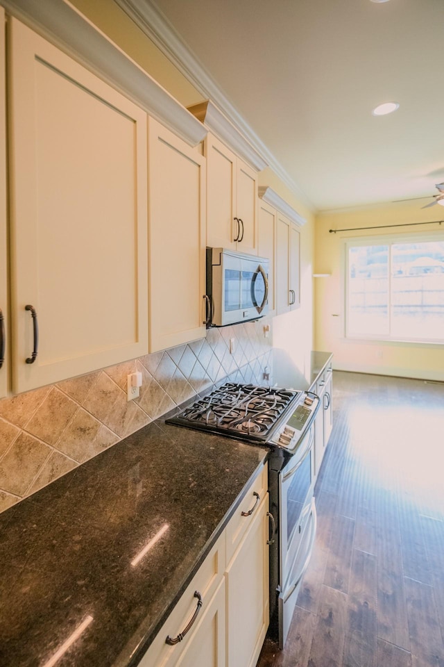 kitchen with tasteful backsplash, ornamental molding, appliances with stainless steel finishes, dark stone counters, and white cabinets