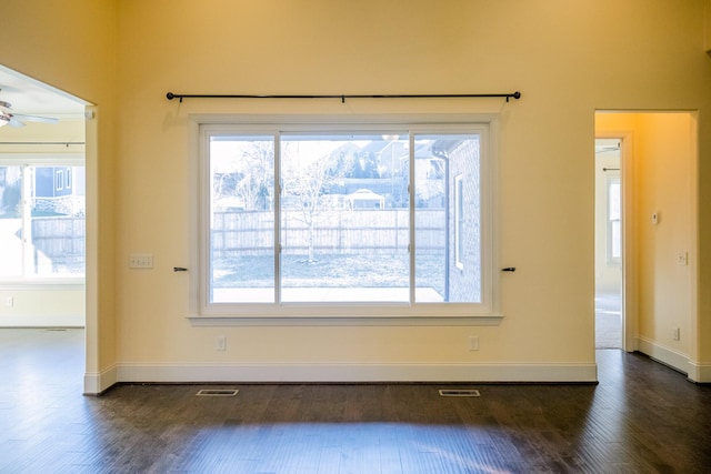 empty room featuring plenty of natural light, dark wood-type flooring, and ceiling fan