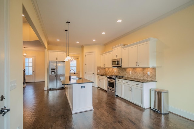 kitchen with pendant lighting, stainless steel appliances, white cabinets, and a center island with sink