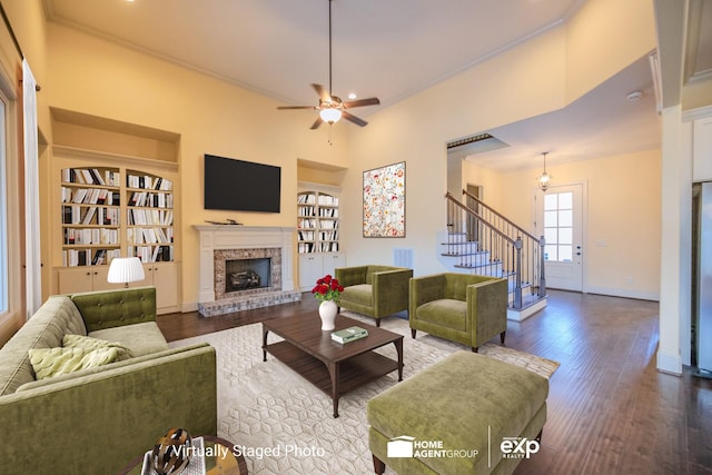 living room with hardwood / wood-style floors, built in features, a fireplace, ceiling fan, and crown molding