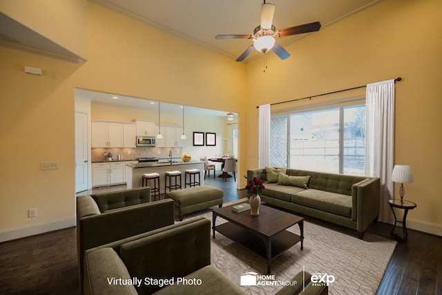 living room with a towering ceiling, sink, dark hardwood / wood-style flooring, ceiling fan, and crown molding