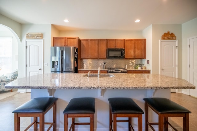 kitchen with appliances with stainless steel finishes, sink, backsplash, a center island with sink, and a breakfast bar area