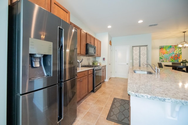 kitchen with hanging light fixtures, sink, backsplash, light stone counters, and stainless steel appliances