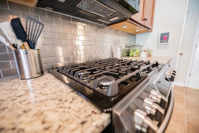 room details with stainless steel stove, backsplash, light stone countertops, and light brown cabinets