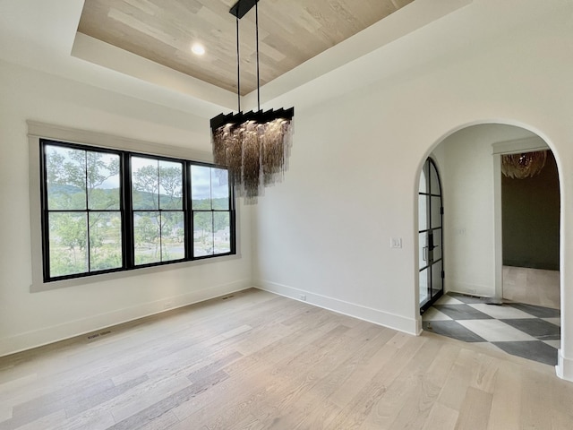 empty room with wooden ceiling, light wood-type flooring, and a raised ceiling