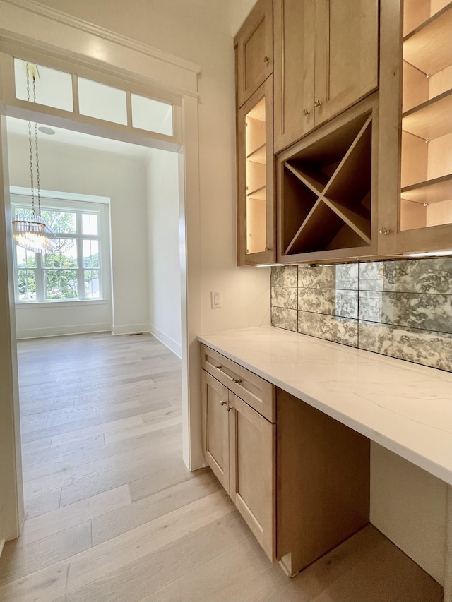 kitchen featuring light stone countertops, built in desk, light hardwood / wood-style floors, backsplash, and hanging light fixtures