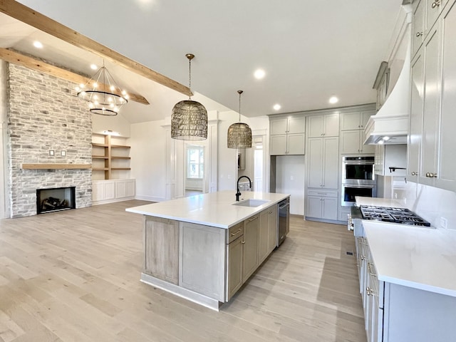 kitchen with stainless steel appliances, a stone fireplace, sink, hanging light fixtures, and a large island