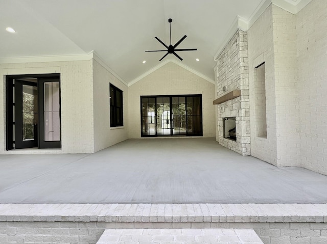 unfurnished living room featuring brick wall, a stone fireplace, ornamental molding, vaulted ceiling, and ceiling fan