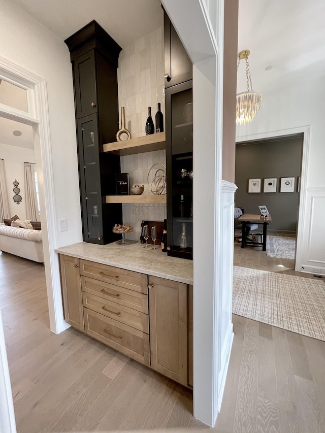 bar with decorative light fixtures, light brown cabinets, an inviting chandelier, and light wood-type flooring