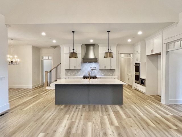 kitchen with decorative light fixtures, custom range hood, and a center island with sink