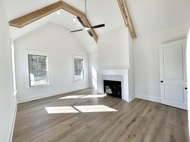 unfurnished living room with light wood-type flooring, beam ceiling, high vaulted ceiling, and ceiling fan