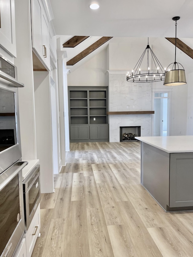 kitchen with light hardwood / wood-style floors, white cabinetry, hanging light fixtures, an inviting chandelier, and lofted ceiling with beams