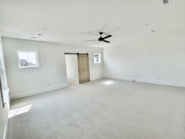 carpeted empty room featuring ceiling fan and a barn door