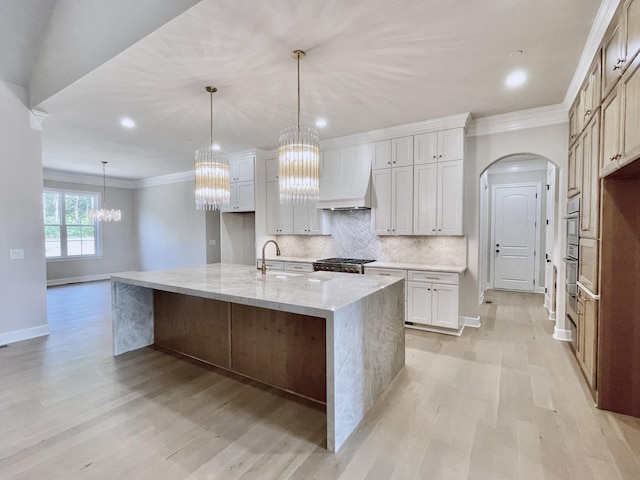 kitchen with decorative light fixtures, white cabinetry, a kitchen island with sink, and custom range hood