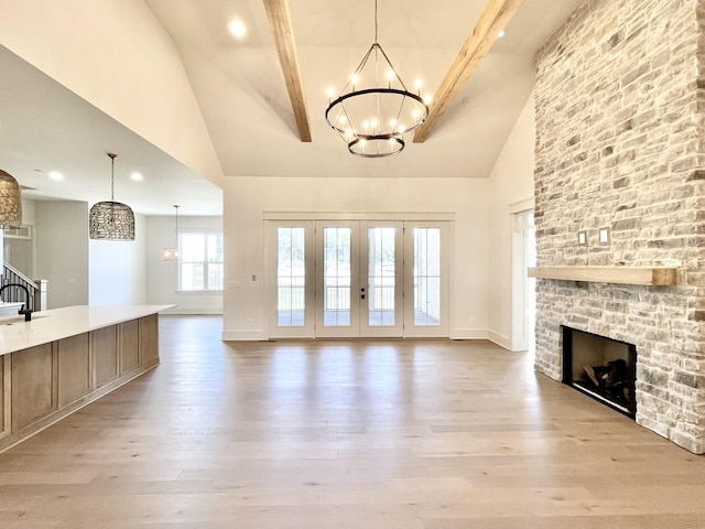 unfurnished living room featuring a towering ceiling, a fireplace, a notable chandelier, light hardwood / wood-style floors, and beamed ceiling