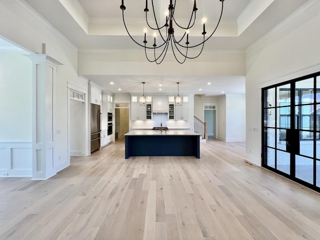 kitchen featuring pendant lighting, white cabinets, an island with sink, stainless steel fridge, and a raised ceiling