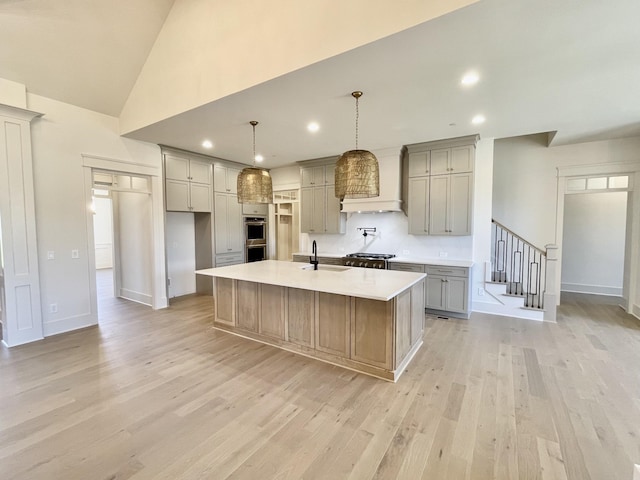 kitchen with custom exhaust hood, decorative light fixtures, sink, gray cabinets, and a center island with sink