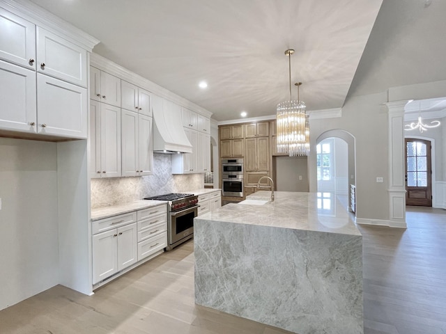 kitchen with white cabinets, stainless steel appliances, custom range hood, and a kitchen island with sink