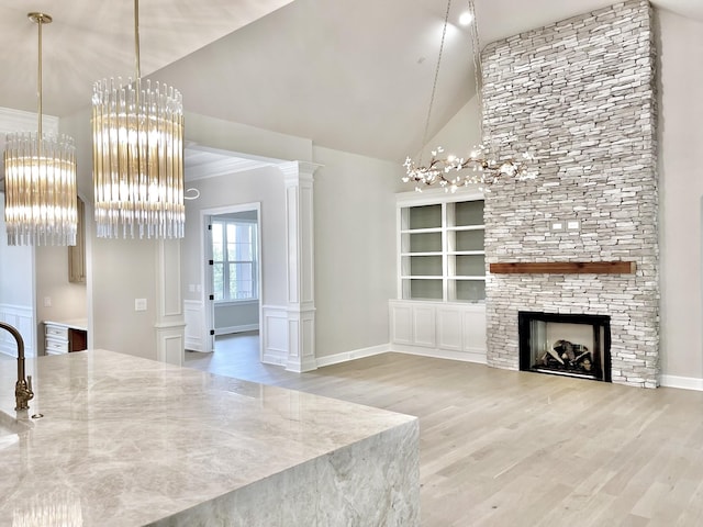 unfurnished living room featuring hardwood / wood-style flooring, a stone fireplace, ornate columns, and lofted ceiling