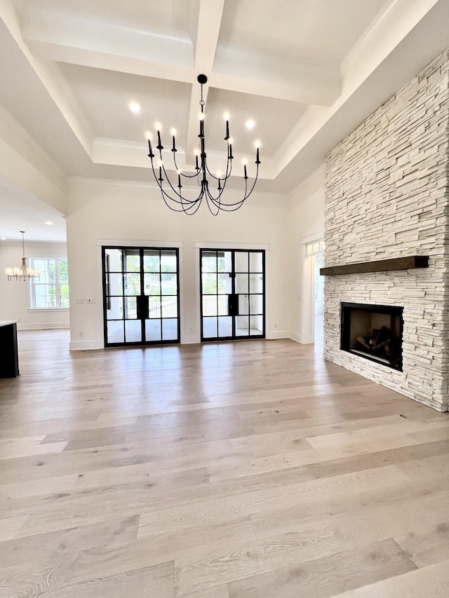 unfurnished living room with a notable chandelier, light wood-type flooring, a stone fireplace, and beam ceiling