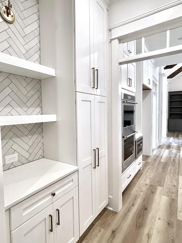 kitchen with white cabinets, light wood-type flooring, and double oven