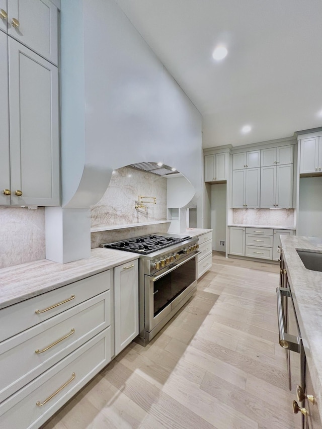 kitchen featuring high end stainless steel range oven, backsplash, light hardwood / wood-style floors, and light stone counters