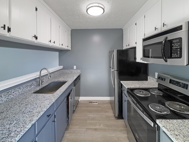 kitchen with a textured ceiling, white cabinetry, stainless steel appliances, sink, and light wood-type flooring