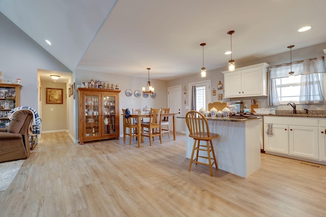 kitchen with pendant lighting, white cabinetry, dark stone counters, light hardwood / wood-style floors, and a kitchen breakfast bar