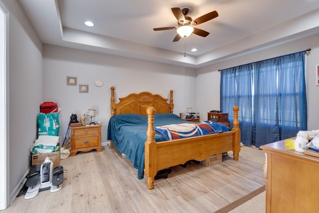 bedroom featuring light wood-type flooring, ceiling fan, and a tray ceiling