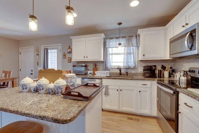 kitchen with a kitchen breakfast bar, hanging light fixtures, appliances with stainless steel finishes, sink, and white cabinetry