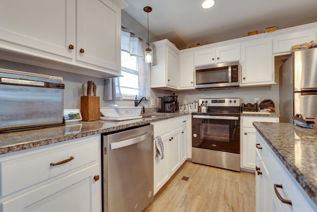 kitchen with light hardwood / wood-style floors, white cabinets, dark stone countertops, pendant lighting, and stainless steel appliances