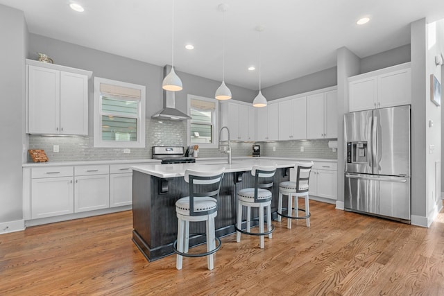 kitchen featuring stainless steel appliances, light countertops, white cabinets, a sink, and wall chimney exhaust hood