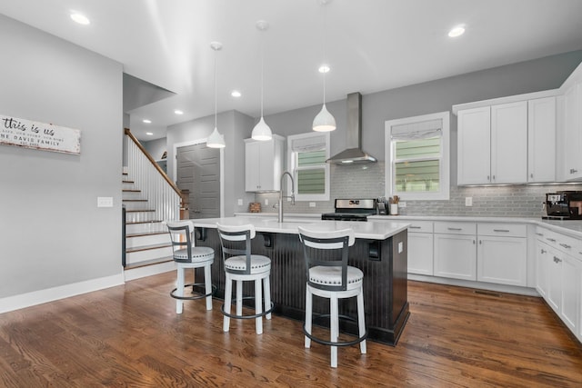 kitchen with stainless steel gas range oven, dark wood finished floors, wall chimney exhaust hood, a kitchen bar, and a sink