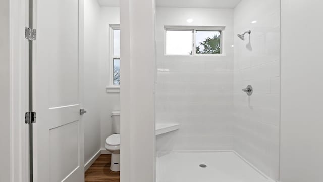 bathroom featuring hardwood / wood-style flooring, toilet, and a tile shower