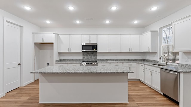 kitchen with appliances with stainless steel finishes, sink, white cabinetry, light stone counters, and a kitchen island