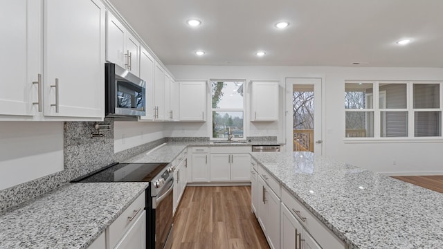 kitchen with appliances with stainless steel finishes, sink, light wood-type flooring, white cabinetry, and light stone counters