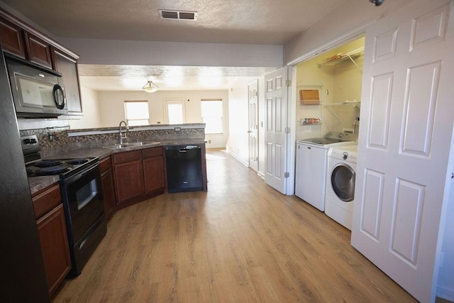 kitchen featuring sink, washer and clothes dryer, light hardwood / wood-style floors, black appliances, and a textured ceiling