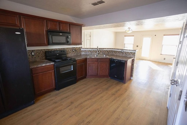 kitchen featuring sink, light hardwood / wood-style flooring, kitchen peninsula, decorative backsplash, and black appliances