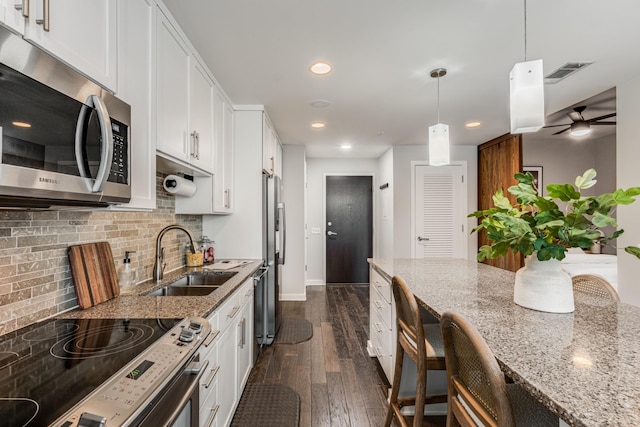 kitchen featuring light stone countertops, white cabinetry, sink, pendant lighting, and stainless steel appliances