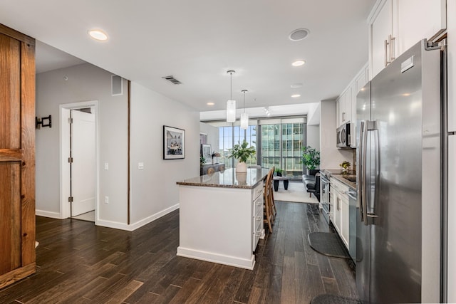 kitchen with appliances with stainless steel finishes, a kitchen island, white cabinetry, dark stone counters, and hanging light fixtures