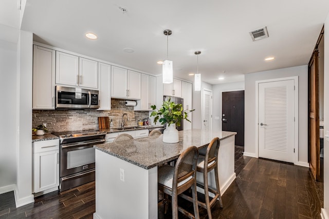 kitchen featuring white cabinets, a kitchen island, stainless steel appliances, dark stone countertops, and hanging light fixtures