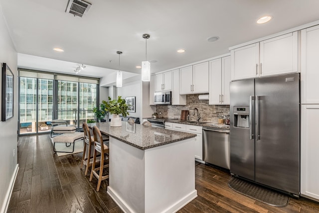 kitchen with a center island, appliances with stainless steel finishes, white cabinets, dark stone countertops, and pendant lighting