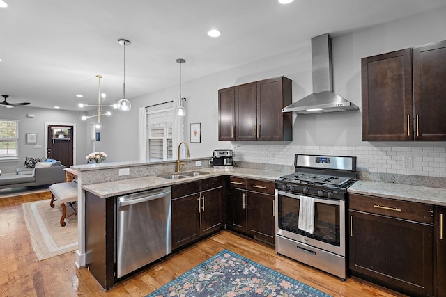 kitchen featuring appliances with stainless steel finishes, wall chimney range hood, decorative light fixtures, sink, and kitchen peninsula