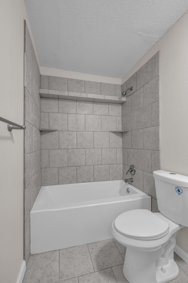 bathroom featuring tile patterned floors, toilet, tiled shower / bath, and a textured ceiling