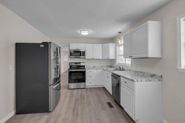 kitchen with light hardwood / wood-style flooring, hanging light fixtures, appliances with stainless steel finishes, white cabinetry, and a textured ceiling