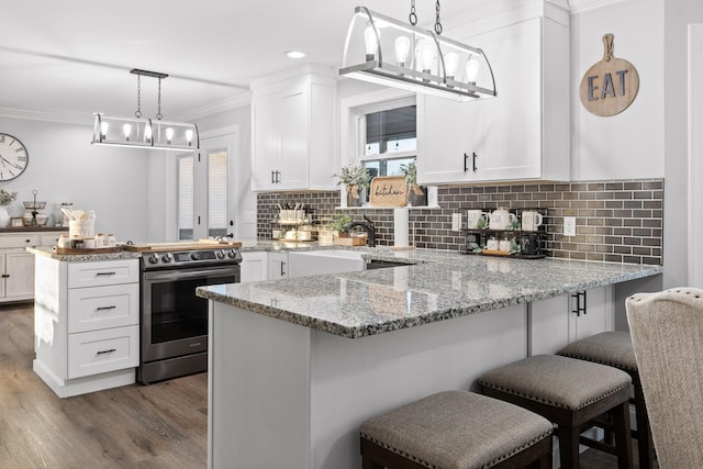 kitchen with light stone countertops, white cabinets, backsplash, electric range, and a breakfast bar area