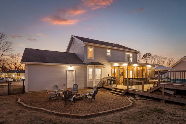 back house at dusk with a wooden deck, an outdoor fire pit, and a sunroom