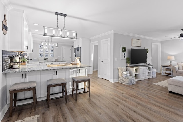 kitchen with kitchen peninsula, ceiling fan, white cabinets, light stone countertops, and a breakfast bar