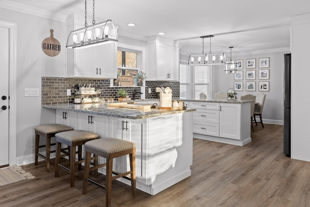 kitchen featuring white cabinets, decorative light fixtures, kitchen peninsula, light stone counters, and a breakfast bar area