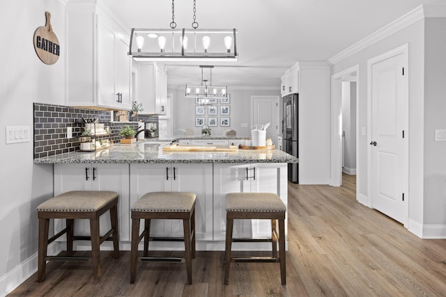 kitchen with light stone countertops, white cabinetry, hanging light fixtures, high end fridge, and kitchen peninsula